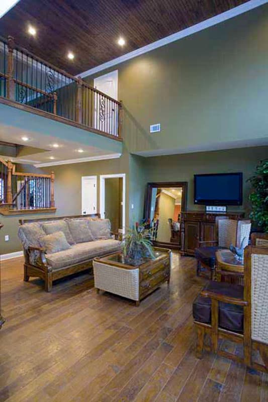 Living room with vaulted wood ceiling, open loft with railing, sofa, coffee table, and television.