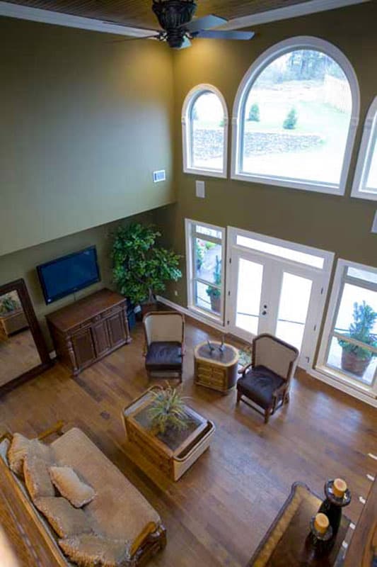 Interior view of a two-story great room with vaulted ceiling, large arched windows, and double doors.