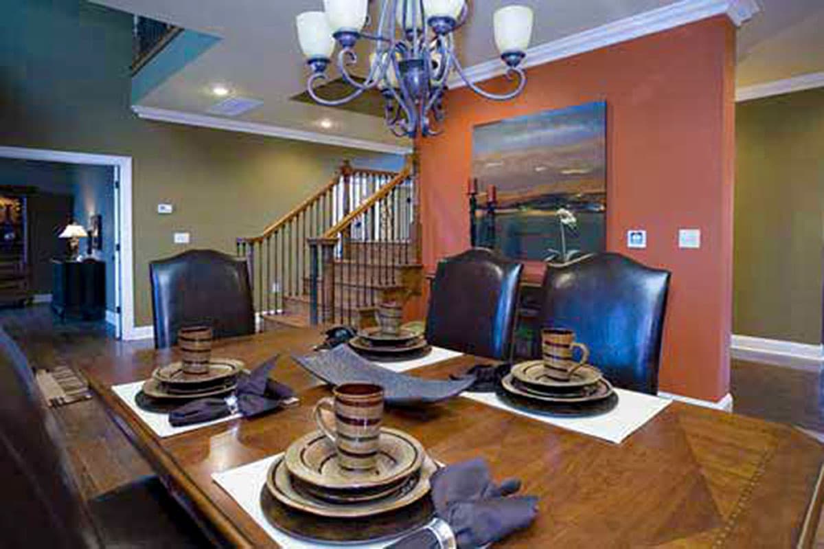 Formal dining room with a wood table, dark leather chairs, a chandelier, and a staircase with a metal balustrade.