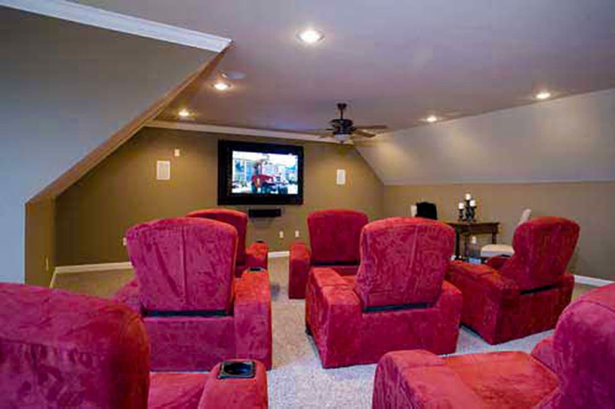 Home theater with red recliners, mounted TV, and sloped ceiling with recessed lighting.