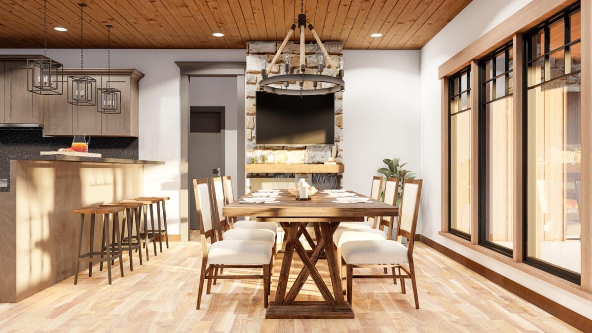 Dining area with stone fireplace and TV, adjacent kitchen with island, and large windows.