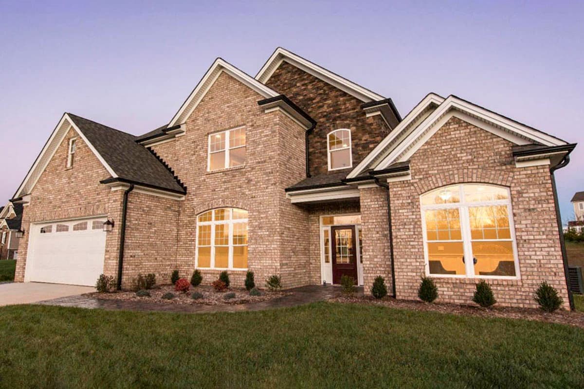 House plan exterior featuring brick facade, prominent gables, arched windows, and a two-car garage.