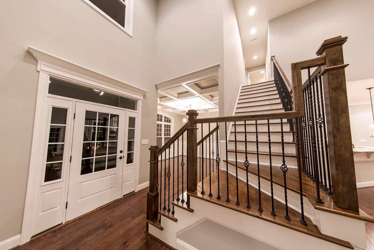 Two-story entryway with double doors, coffered ceiling, and wood staircase with wrought iron spindles.