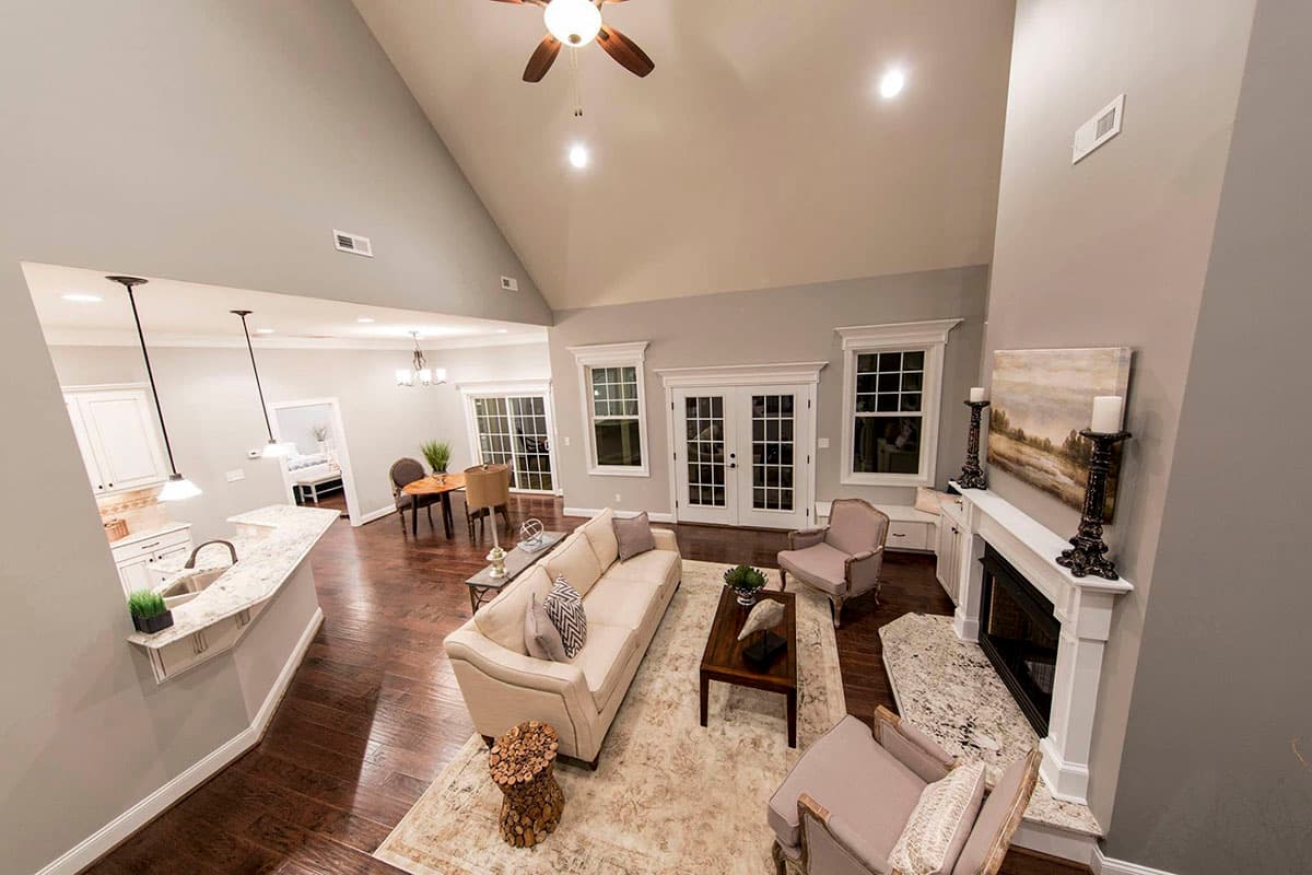 Great room interior with vaulted ceiling, fireplace, kitchen island, and double doors leading outside.
