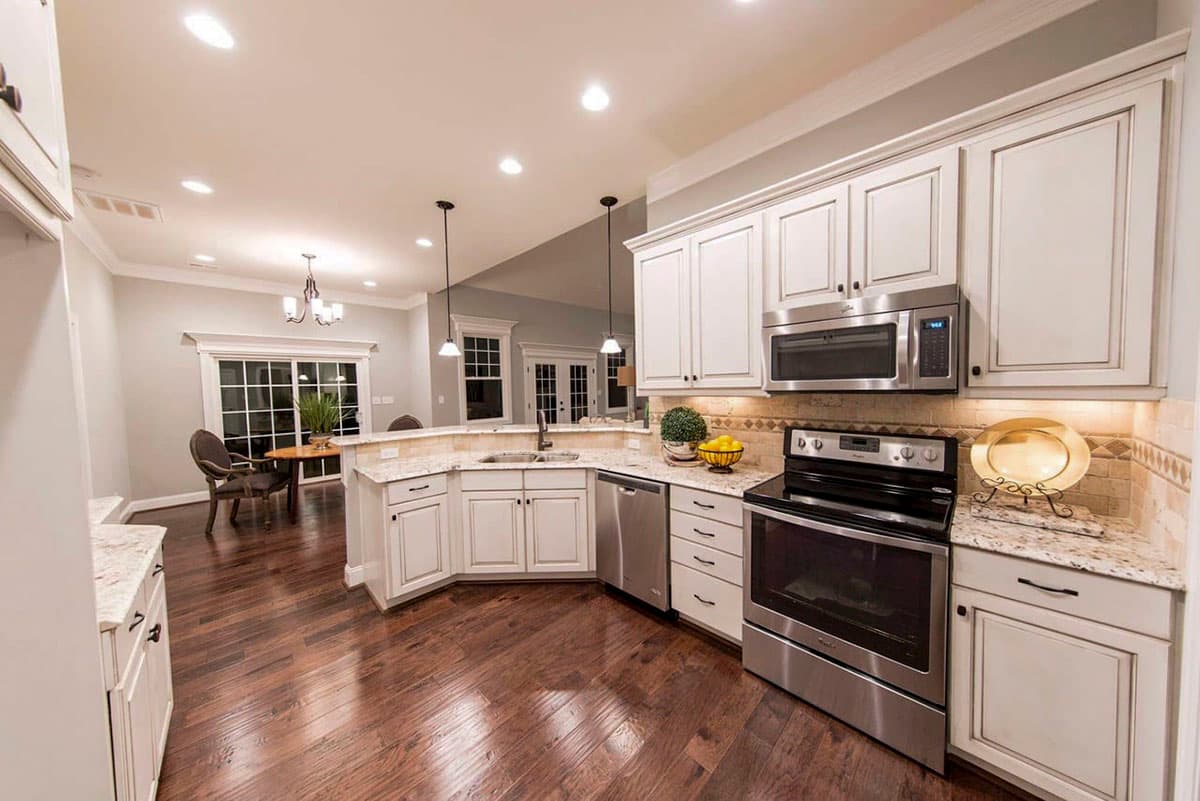 Kitchen with white cabinetry, granite countertops, stainless steel appliances, island, and view of dining area.