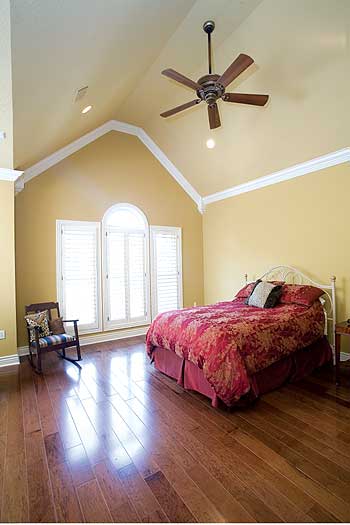 Bedroom with vaulted ceiling, large arched window with shutters, ceiling fan, and wood flooring.