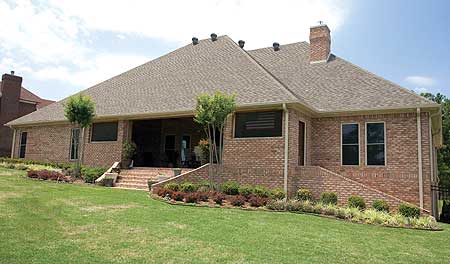 House plan exterior shows brick facade, gabled roof, covered patio, and stepped brick retaining walls.