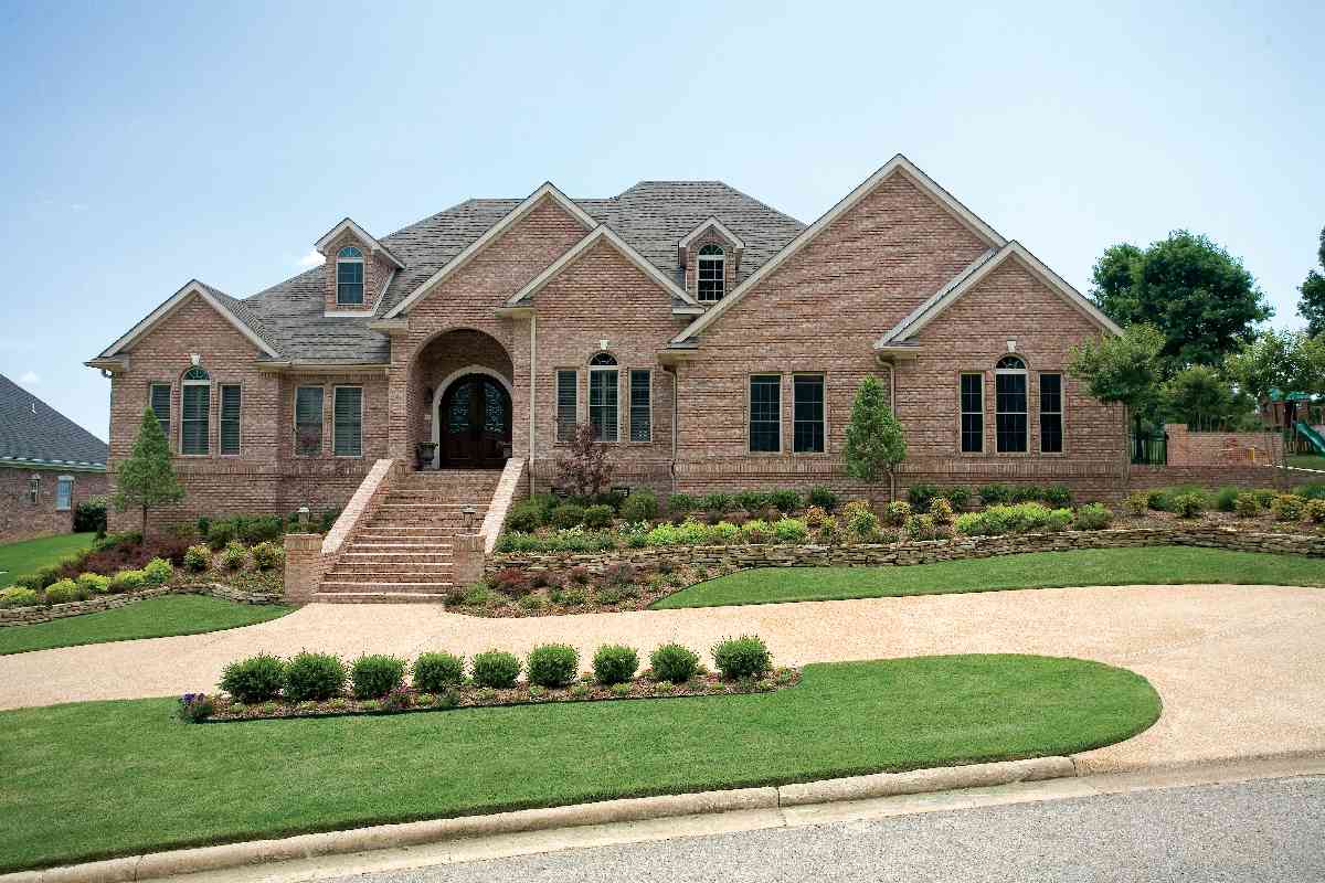 Brick house plan exterior with arched entry, multiple gables, dormers, and multi-level rooflines.