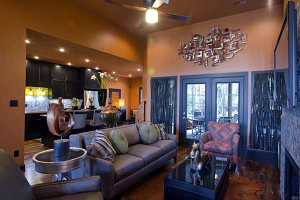 Living room with vaulted ceiling, dark kitchen cabinets, fireplace, and double doors leading outside.