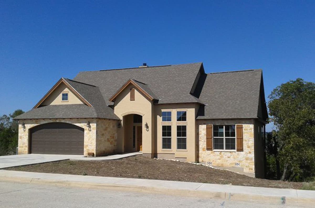 House plan exterior: One-story home with stone accents, arched garage, gable dormer, and multiple rooflines.