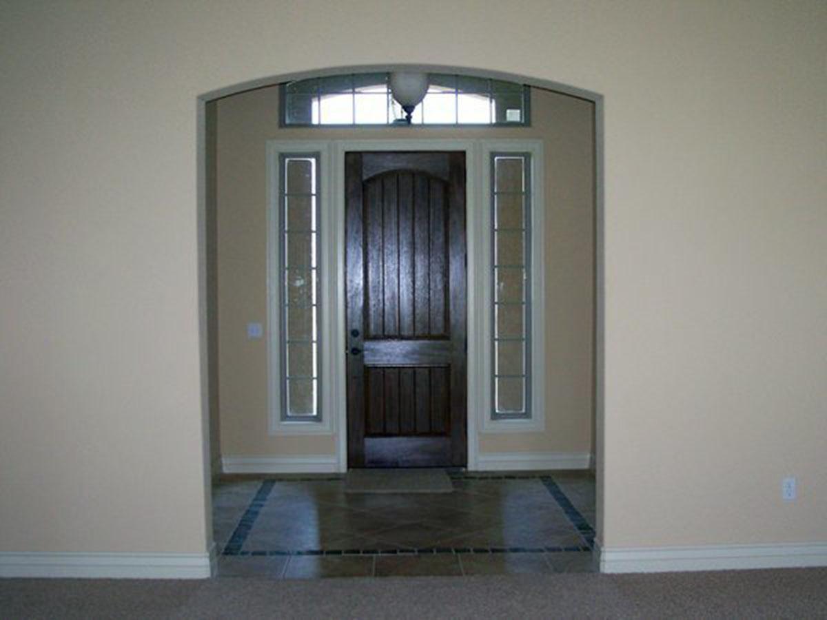 Interior view of arched entryway with dark wood door, sidelights, transom window, and tiled floor.
