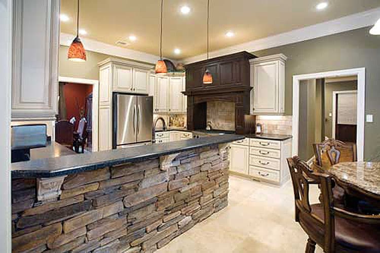 Kitchen with stacked stone island, dark wood range hood, stainless steel refrigerator, and cream cabinetry.