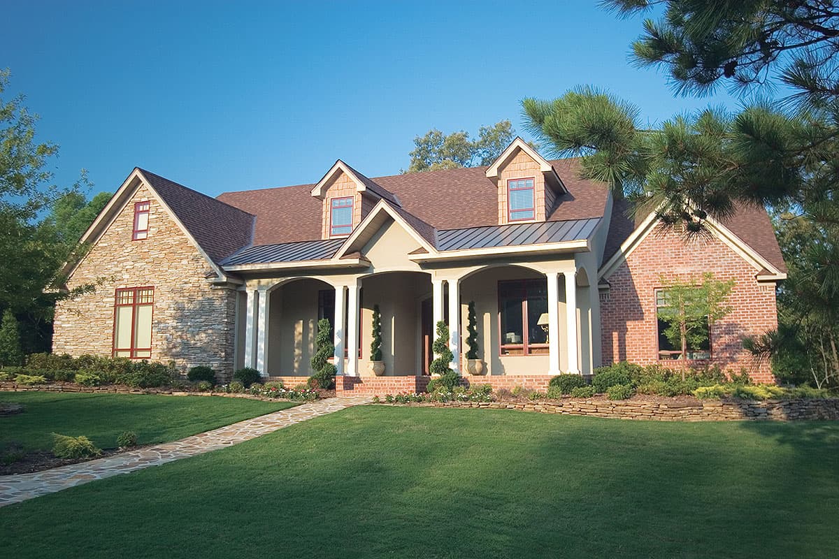 House plan exterior with stone and brick facade, covered arched entry porch, dormers, and multi-level rooflines.
