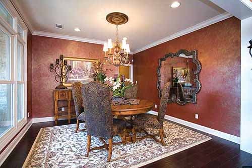 Dining room with round table, ornate chandelier, decorative mirror, and large windows.