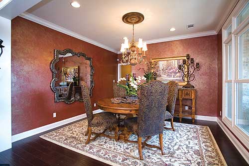 Dining room with round table, upholstered chairs, ornate mirror, chandelier, and large windows.