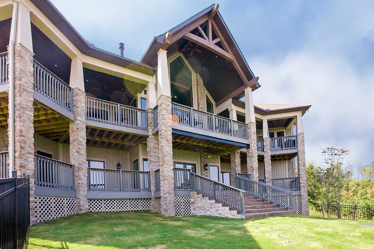 House plan exterior with multiple levels of balconies, stone pillars, a prominent gable with exposed beams, and large windows.