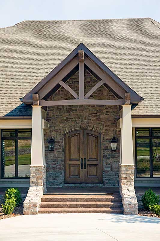 House plan exterior with stone base, wood double doors, covered entry with exposed timber framing, and pitched roof.