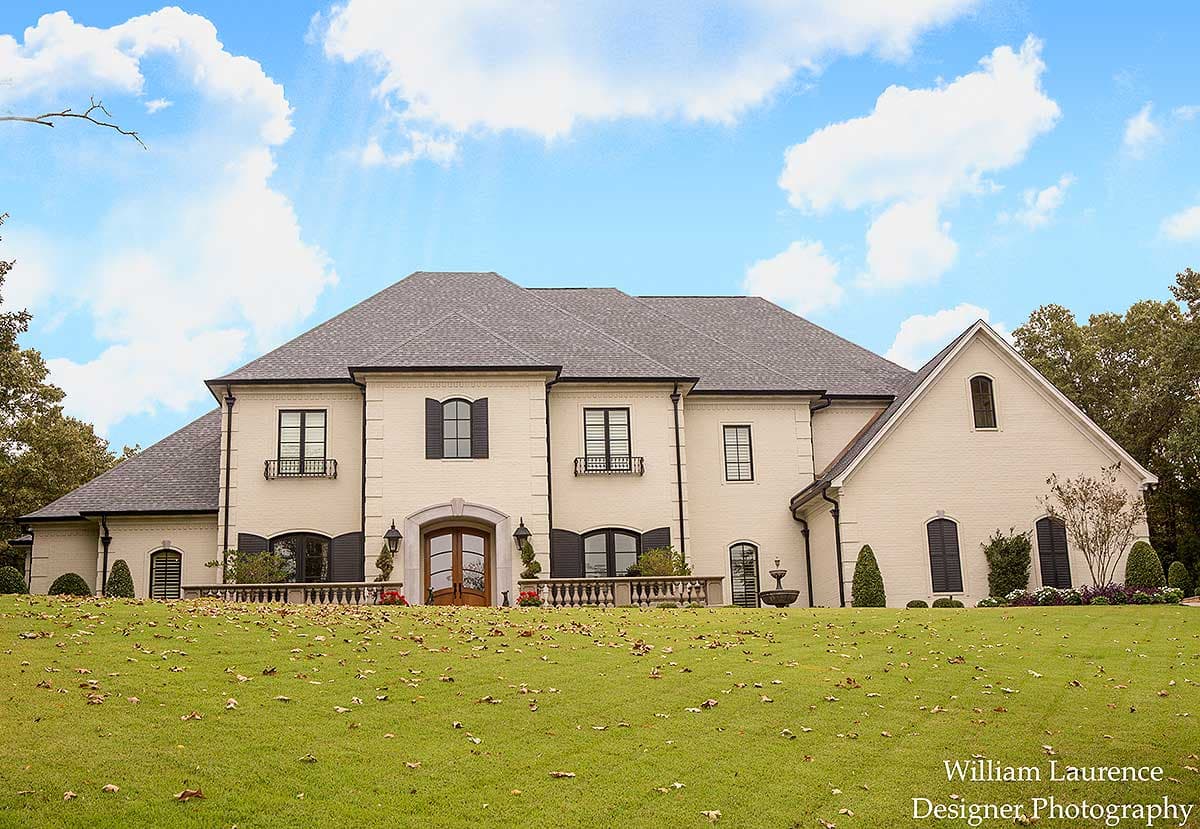 House plan exterior of a two-story French Provincial home with a pitched gray roof, brick facade, arched entryway, and numerous windows.