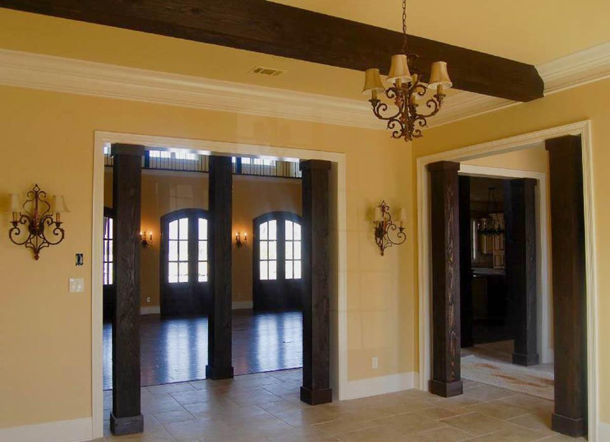 Interior view showing decorative dark wood beams, columns, a chandelier, and arched doorways leading to a room with dual arched doors.
