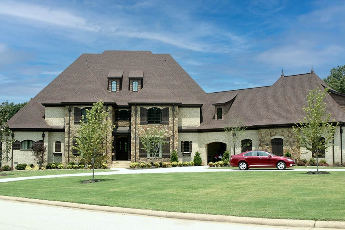 House plan exterior: Two-story estate with stone and brick facade, multiple gables, dormer windows, and a three-car garage.