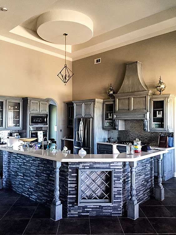 Kitchen with multi-level island featuring stone base and decorative metal wine rack. Contemporary pendant light hangs from a circular ceiling detail.
