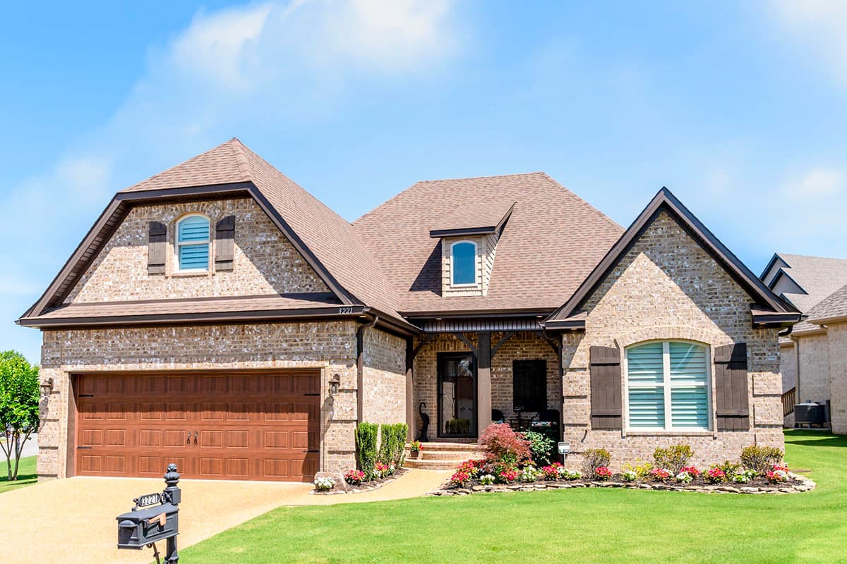 House plan exterior: Two-story brick home with a prominent gabled front, covered entry, dormer, and a two-car garage.