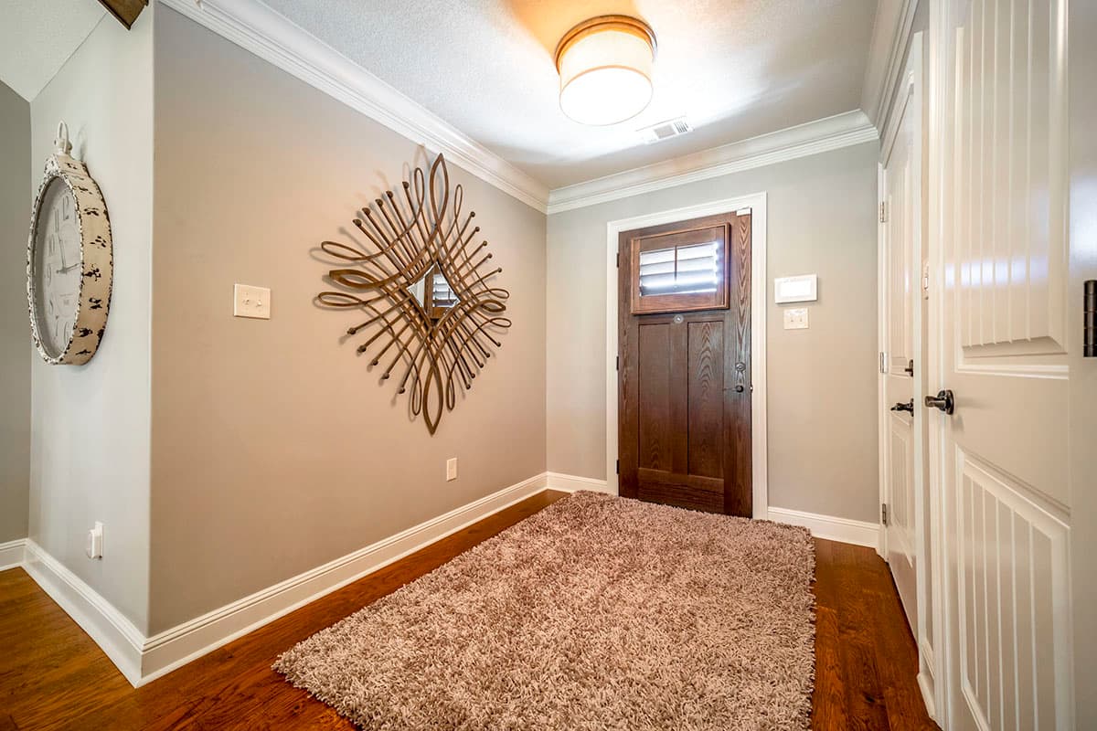 Interior view of entryway with wooden door, decorative mirror, and double-paneled doors.