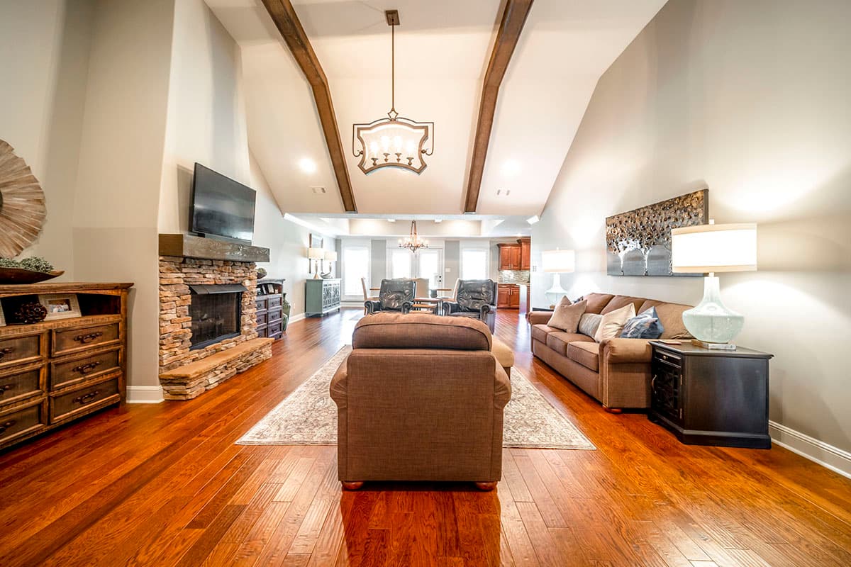 Living room with vaulted ceiling, exposed beams, stone fireplace, and view into dining and kitchen areas.