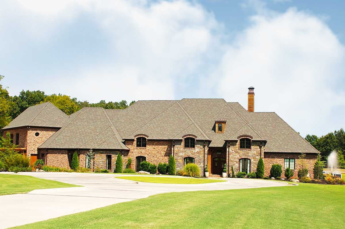 House plan exterior. Two-story, European-style home with gabled roof, brick and stone facade, and arched windows.