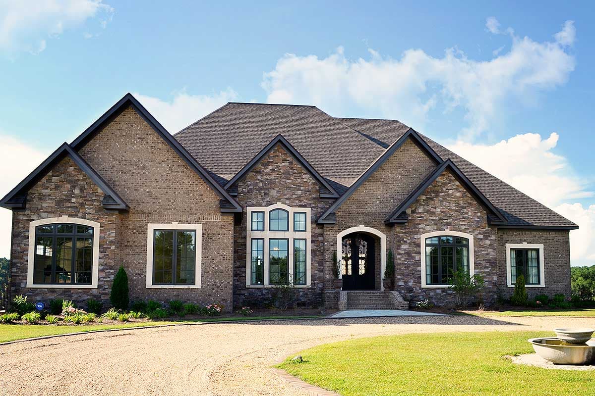 House plan exterior of a one-story brick home with stone accents, multiple gables, and arched entryway with decorative iron door.