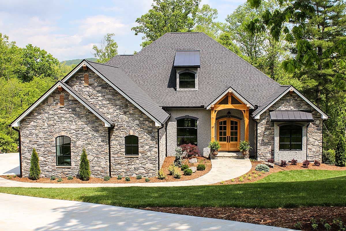 House plan exterior with stone veneer, wood entry porch, and arched windows. Features gabled roofline and eyebrow dormer.
