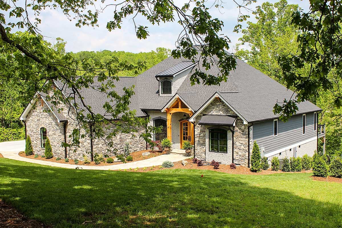 House plan exterior with stone and siding, prominent gables, arched dormers, and a timber-framed entrance.