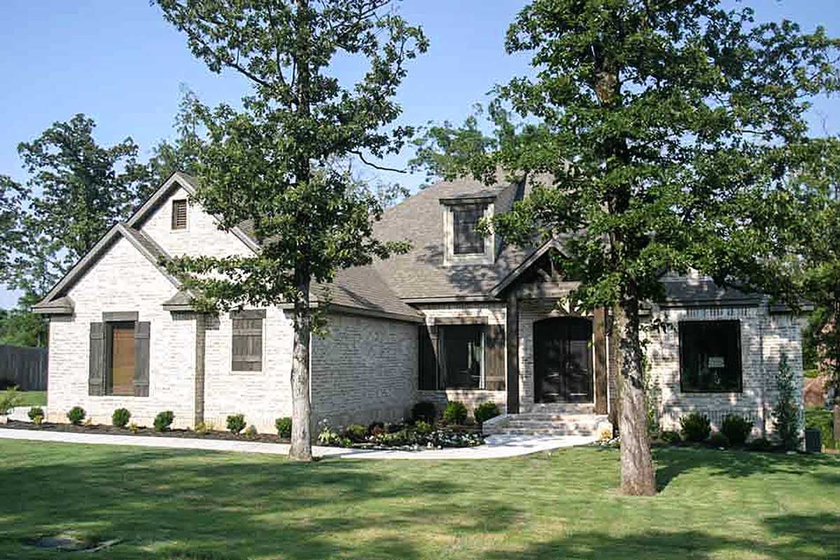House plan exterior: One-story home with white brick, multiple gables, dormer window, and covered entry with wooden beams.