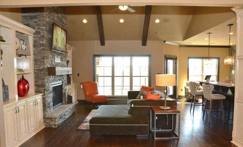 Interior view: Great room with stone fireplace, vaulted ceiling with beams, large window, and kitchen island with bar stools.