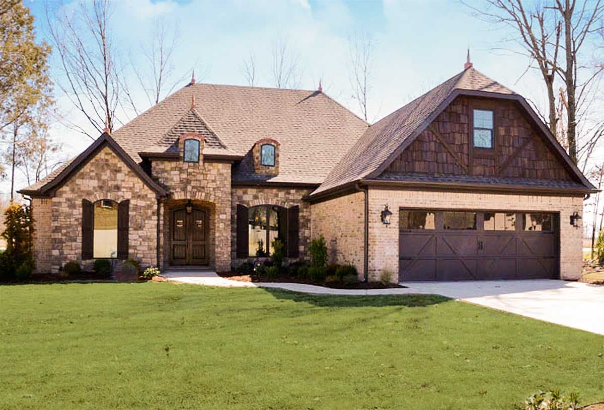 House plan exterior: Two-story home with stone and brick facade, arched entry, dormers, and a side-facing garage.