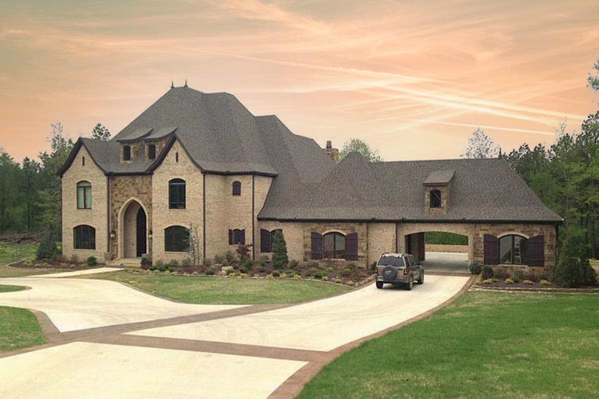 Exterior view of a two-story house plan with stone facade, arched entryway, multiple gables, and a drive-through garage.