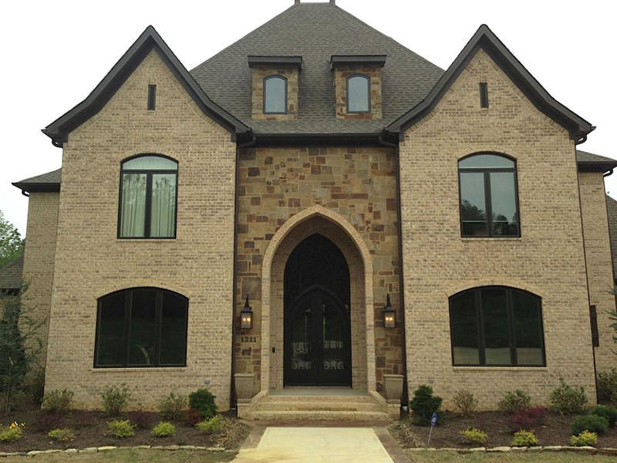 House plan exterior: Two-story brick home with prominent gables, arched entry, stone accents, and dormer windows.