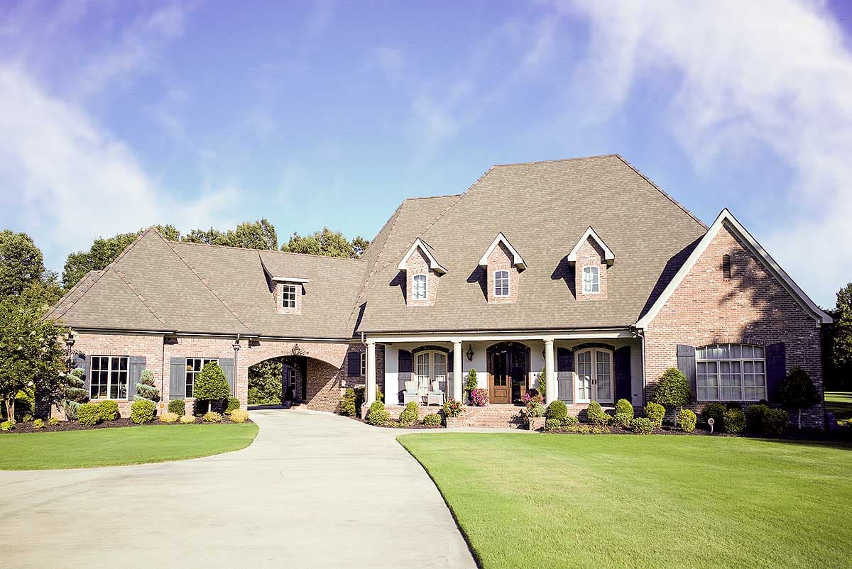 House plan exterior: Two-story brick home with central arched drive-through, dormers, and covered front porch with columns.