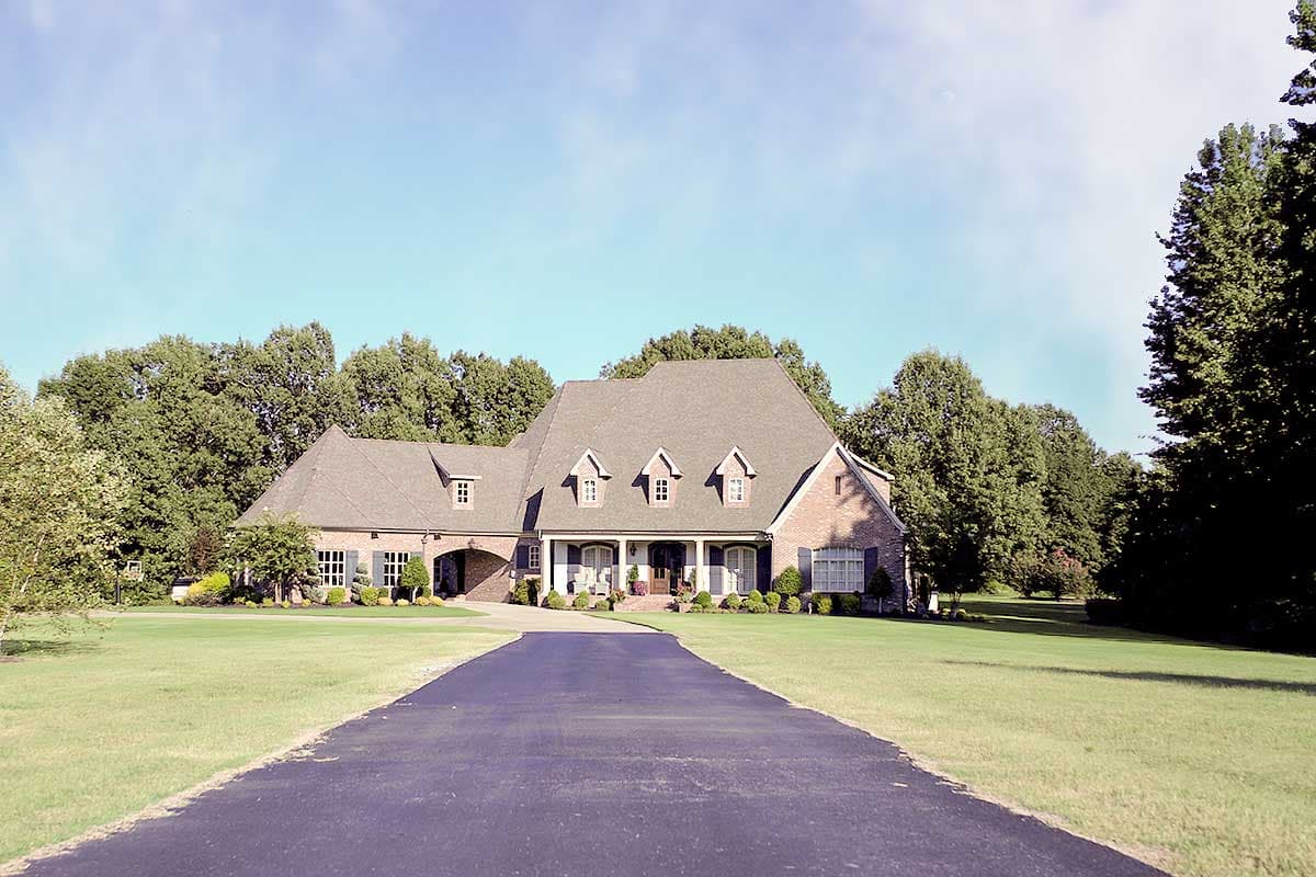 House plan exterior: Two-story brick home with a pitched roof, multiple gables, dormers, and a covered front porch with columns.