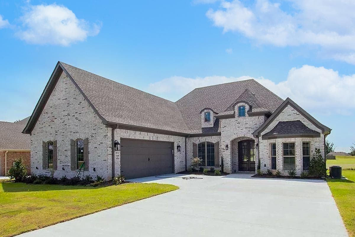 House plan exterior. Two-story brick home with gabled roof, dormers, and attached garage. Driveway leads to arched entry.