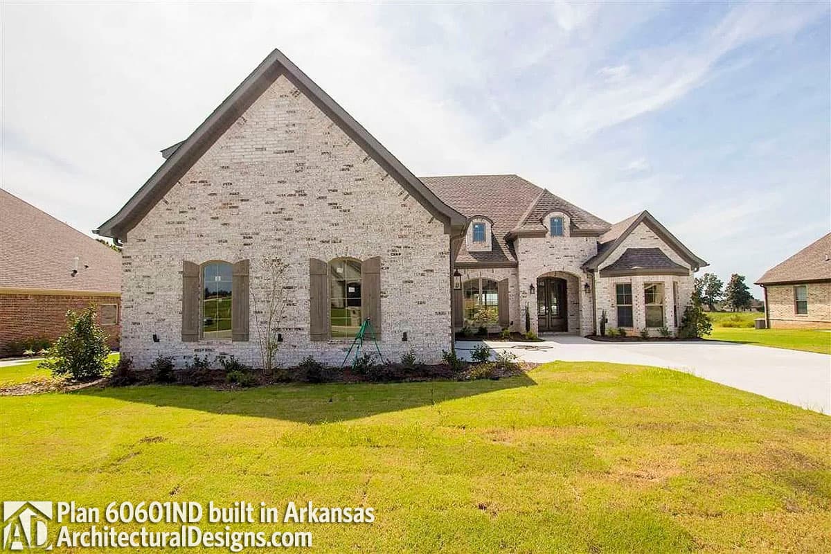 House plan exterior: one-story home with white brick, arched windows, prominent gables, and dormers.