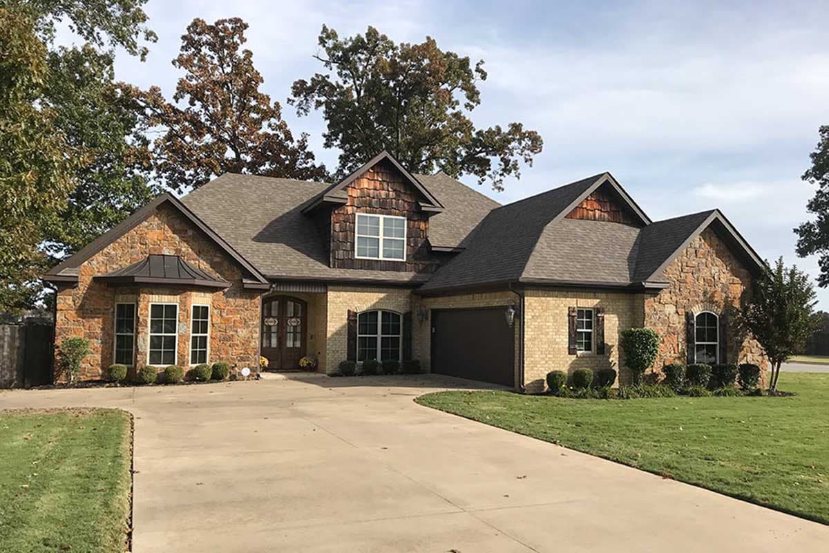 House plan exterior shows a one-story home with stone and brick accents, a prominent dormer, and a side-entry garage.