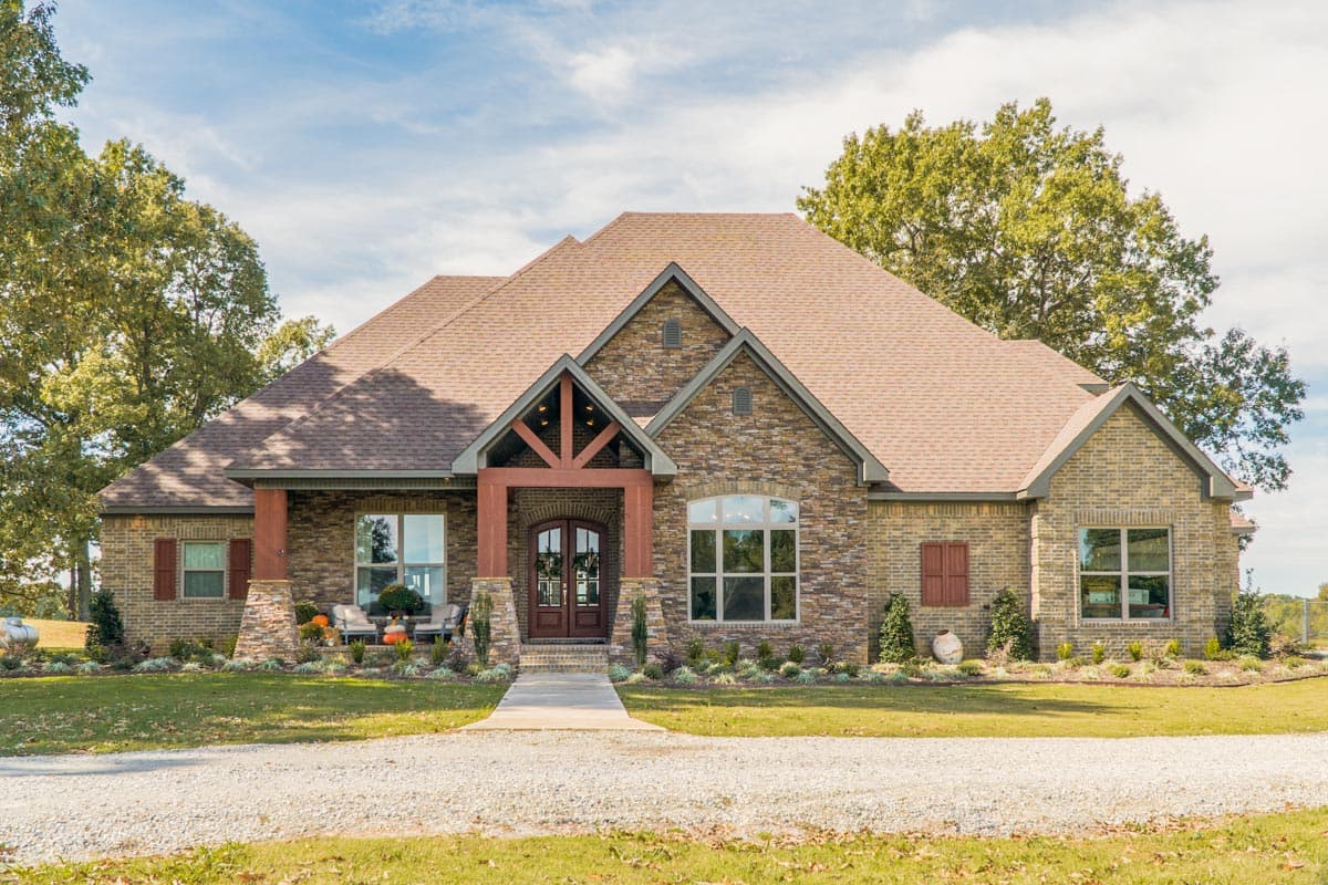 House plan exterior with stone and brick facade, covered entry with wooden beams, and gable rooflines. One-story design.