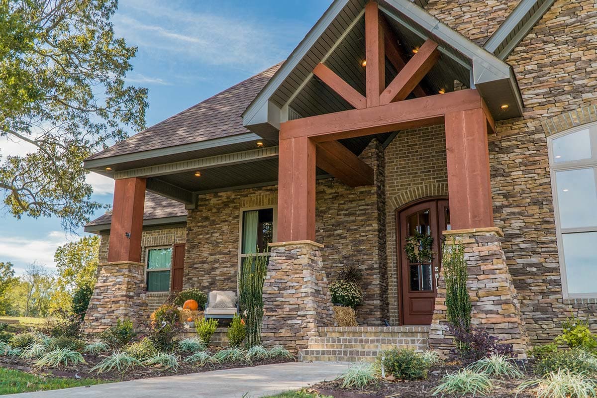 House plan exterior with stone facade, prominent timber-framed gable over porch, and arched double entry door.
