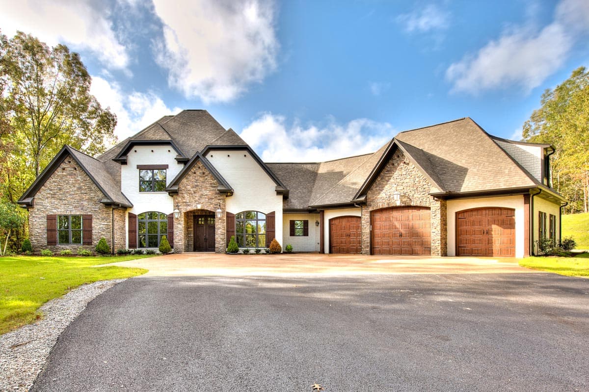 House plan exterior. Two-story with stone and stucco facade. Features include multiple gables, arched windows, and a three-car garage.