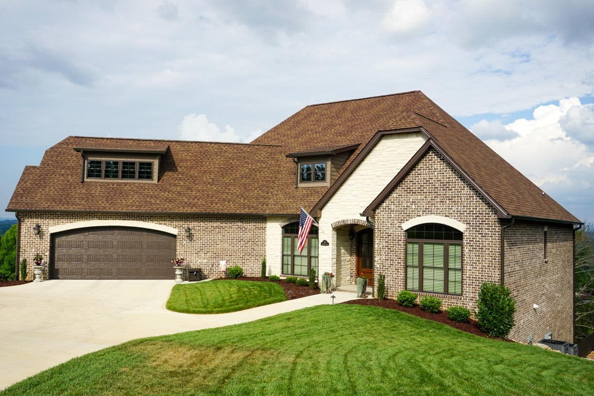 House plan exterior with brick facade, multi-gabled roof, and arched windows. Features a 2-car garage and dormer windows.