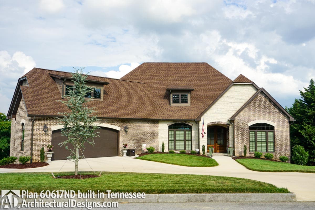 House plan exterior with brick and stone, multiple gables, dormers, and attached side-entry garage.