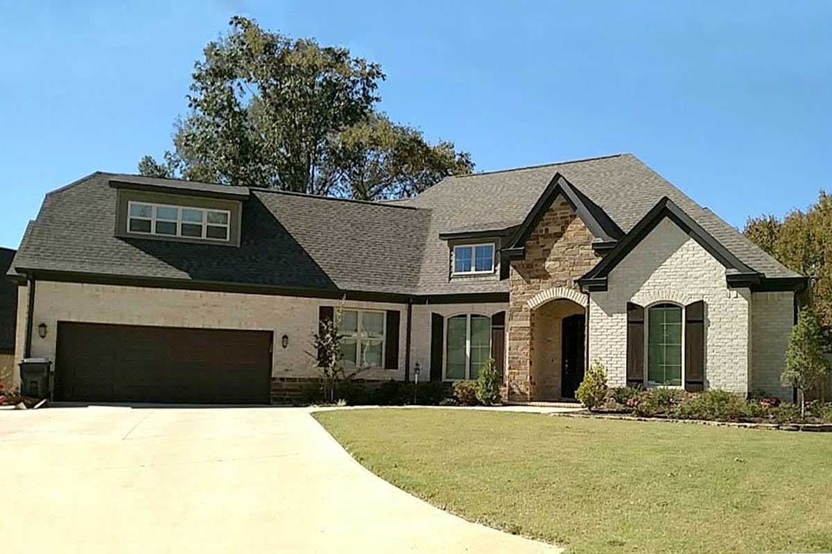 House plan exterior: Two-story, white brick and stone, with a dormer, gabled roof, and attached three-car garage.