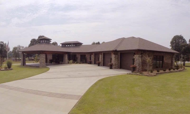 House plan exterior: single-story ranch with stone accents, covered porte-cochère, and four-car garage.