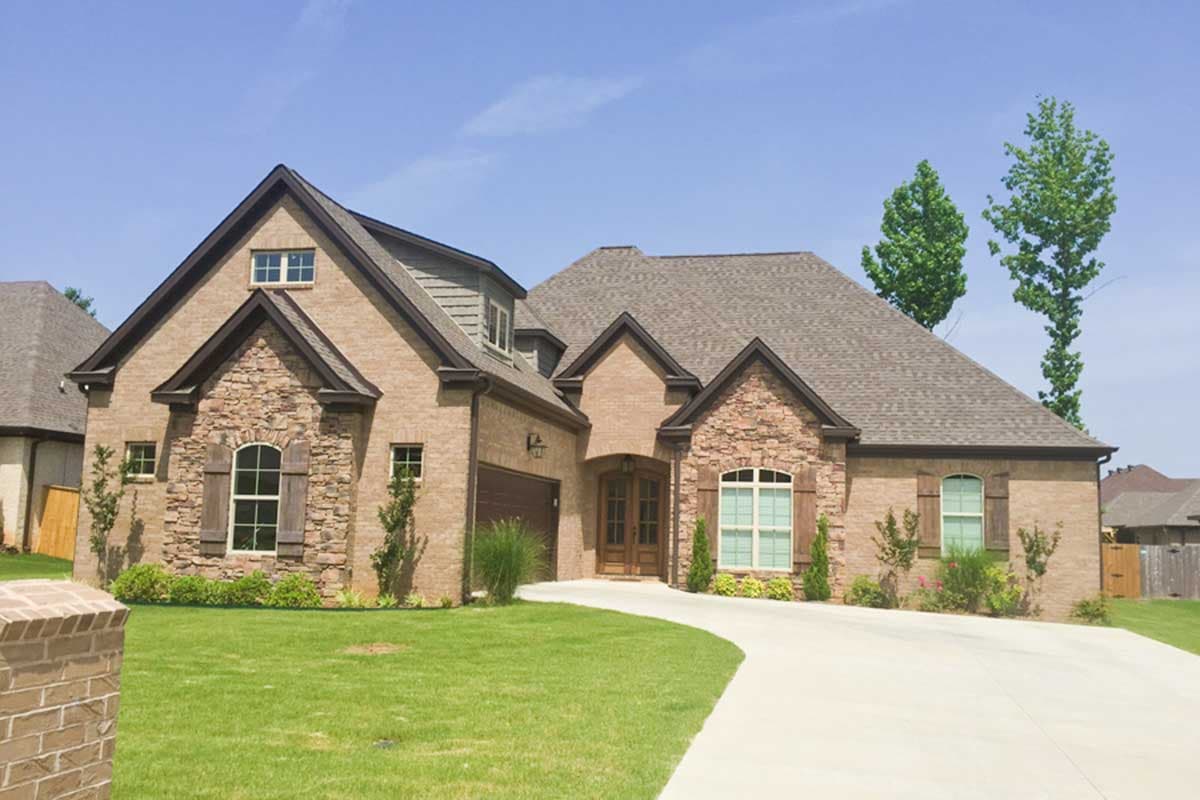 House plan exterior: Brick and stone veneer, two stories, gabled roof with dormers, side-entry garage, arched windows.